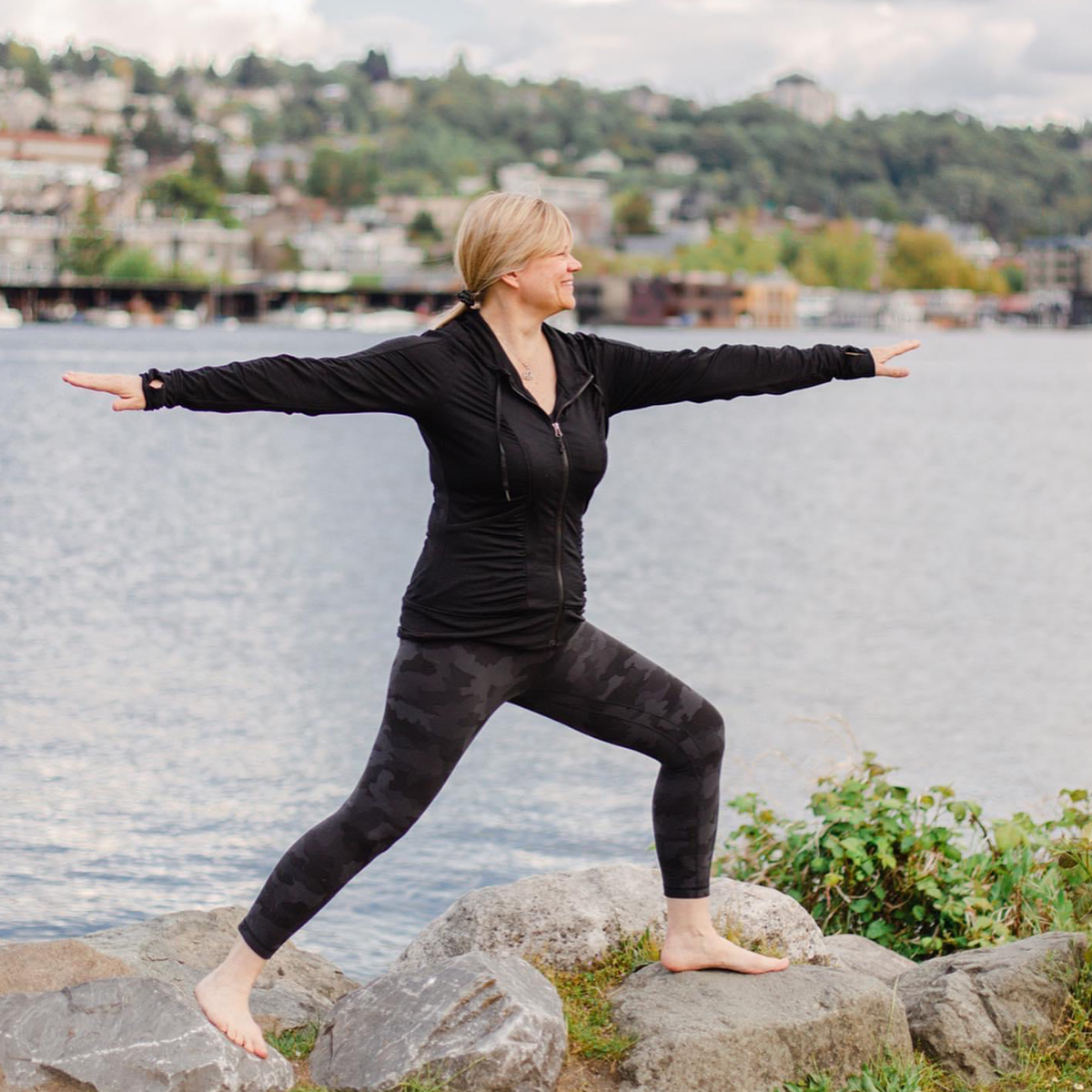 Christa doing Warrior II on rocks outside on edge of Lake Union