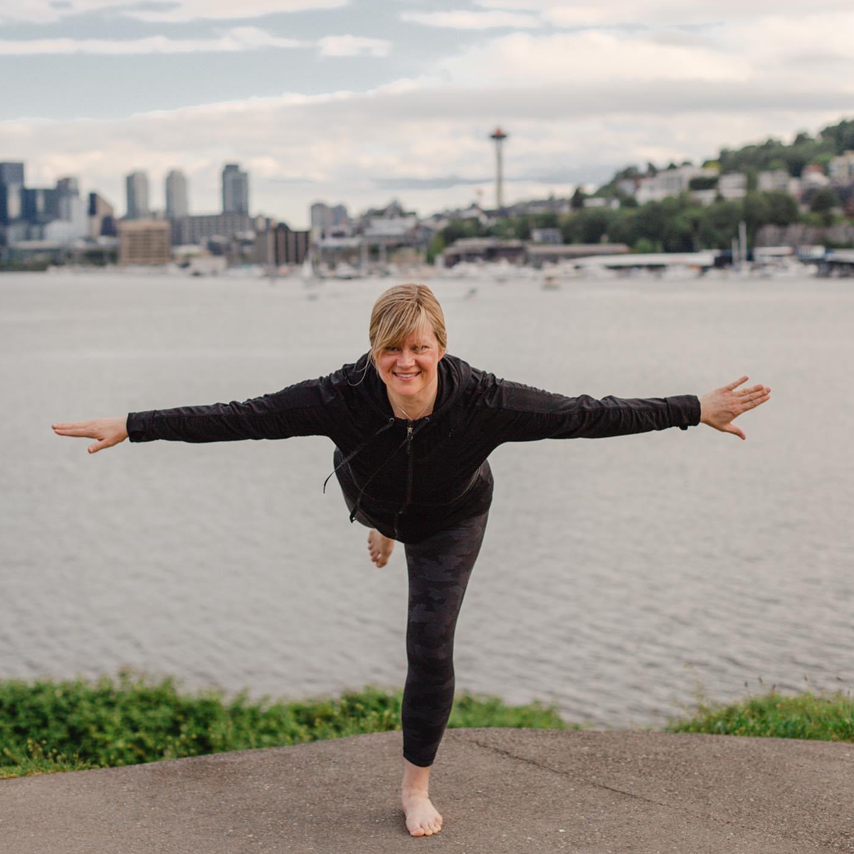 Christa doing Warrior III outside with Seattle space needle behind her in distance