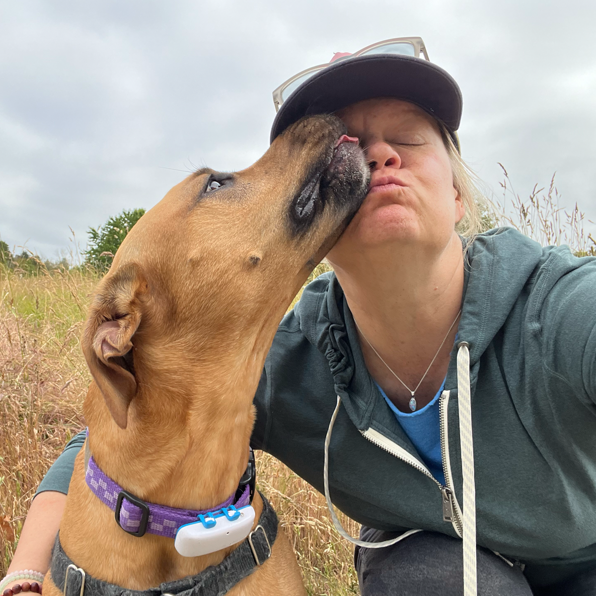 Christa making a kissing face while her dog Rikka licks her on the nose.