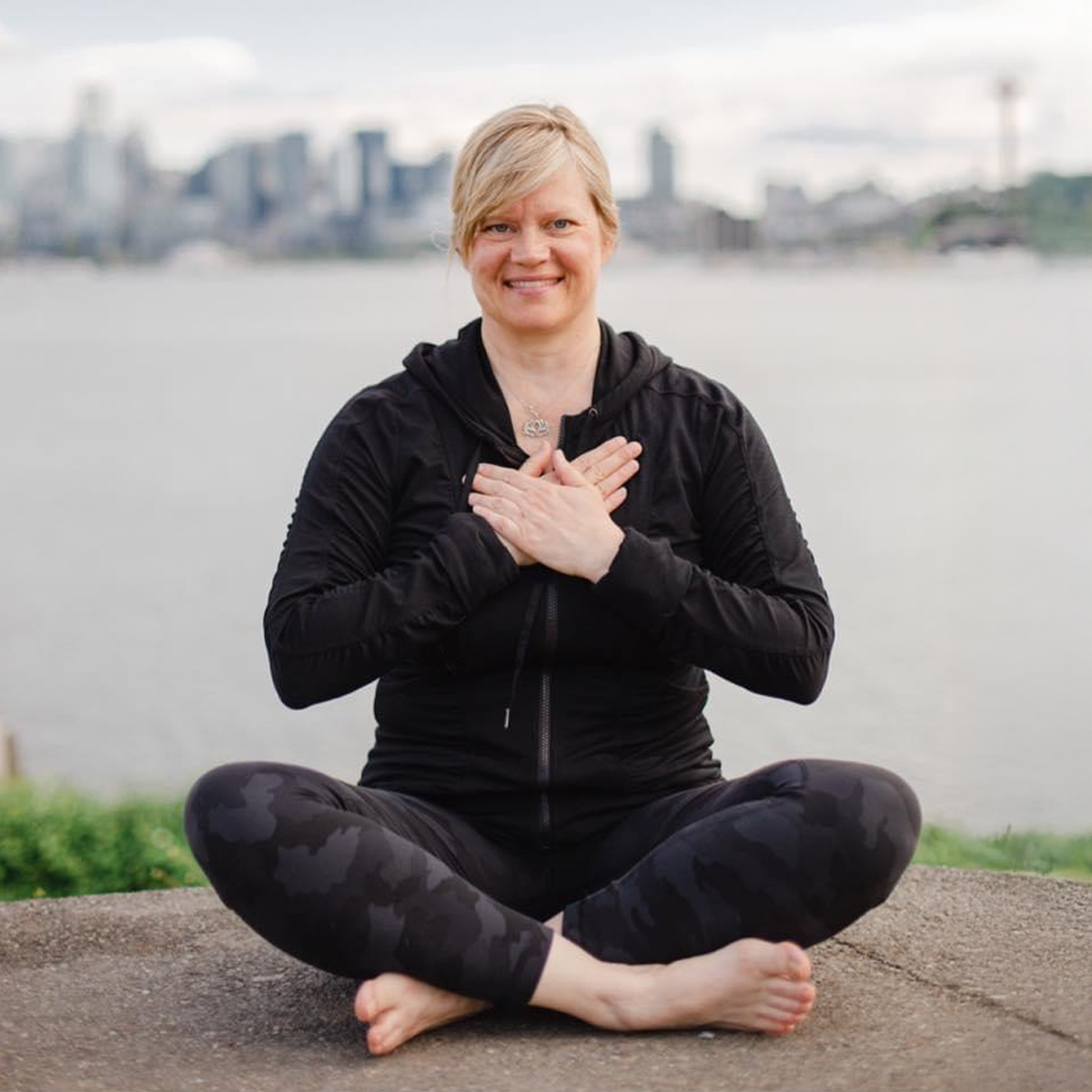 Christa sitting in lotus and smiling at camera with hands over heart