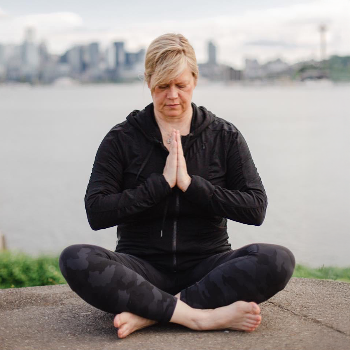 Christa with gaze looking down and sitting in lotus with hands in prayer